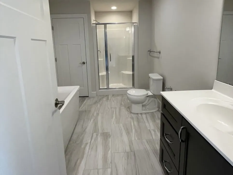 A bathroom featuring dark shaker-style vanity cabinets, a white soaking tub, and white door casing.