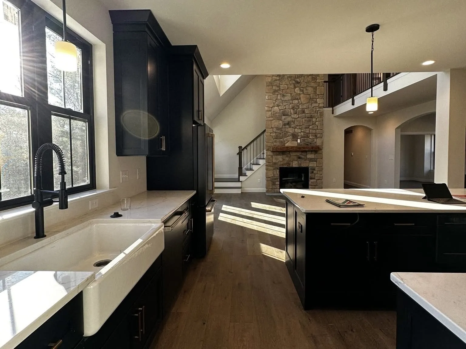 Black kitchen cabinetry with a large island and white countertops overlooking a stone fireplace.