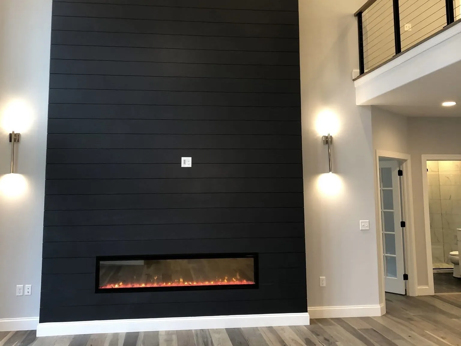 A tall black shiplap accent wall featuring a modern linear electric fireplace in a living room.