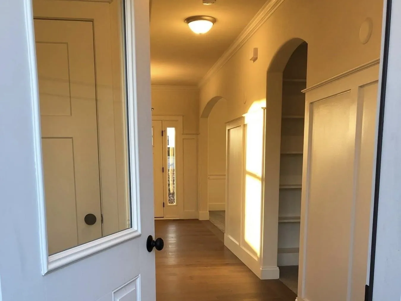 A hallway featuring board and batten wall paneling, arched openings, and built-in shelving units.