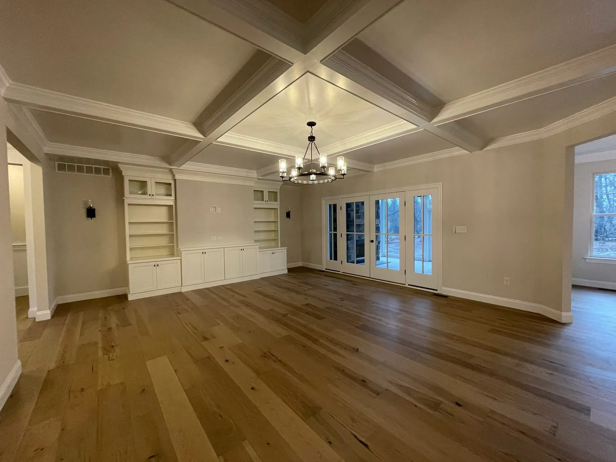 A family room featuring a white coffered ceiling and built-in shelving units with cabinets.