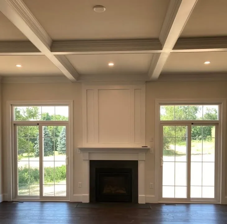 A white coffered ceiling and a fireplace with a wood mantel surround in a room.