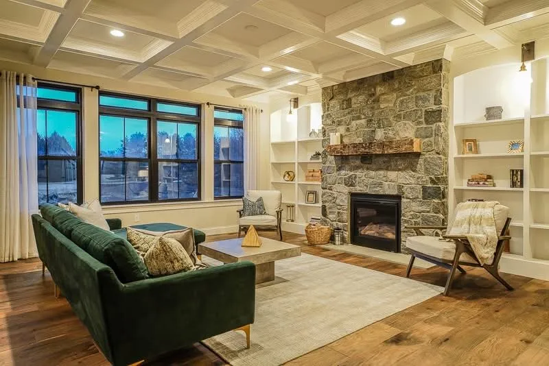 A coffered ceiling sits above a stone fireplace flanked by white built-in shelving units.