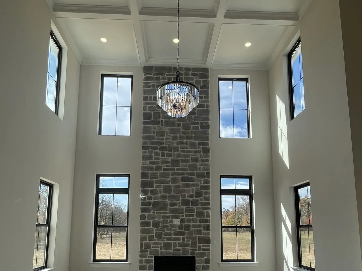 A two-story living room features a tall stone fireplace and a white coffered ceiling design.