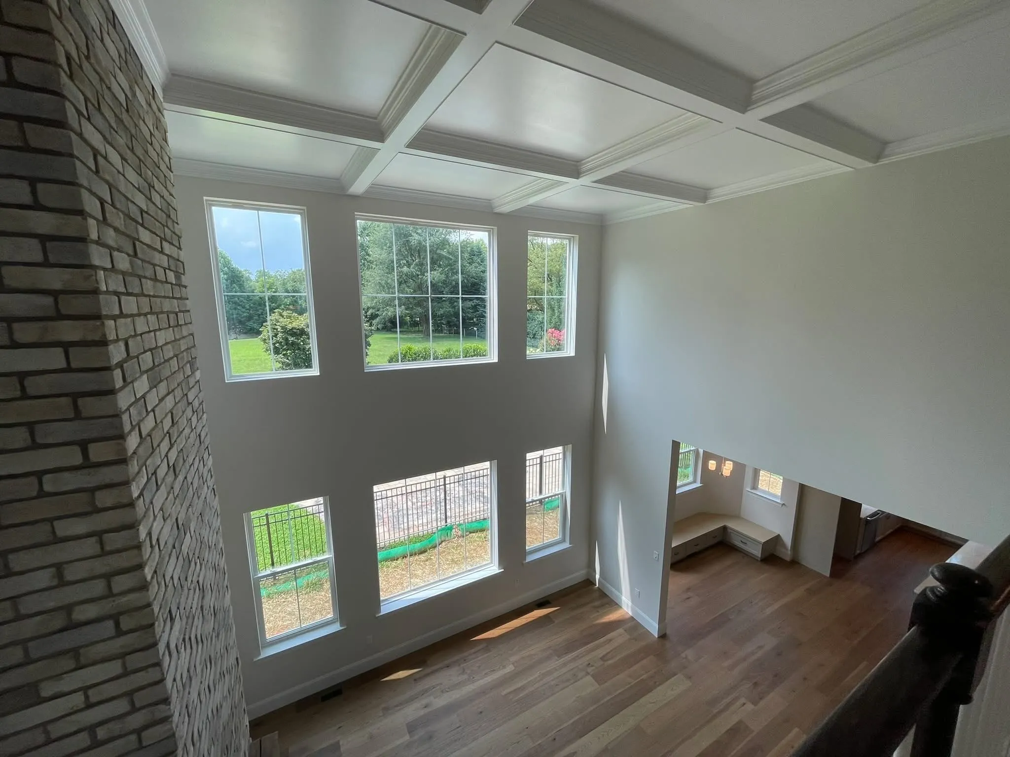 A two-story living room featuring a white coffered ceiling and a tall brick fireplace surround.