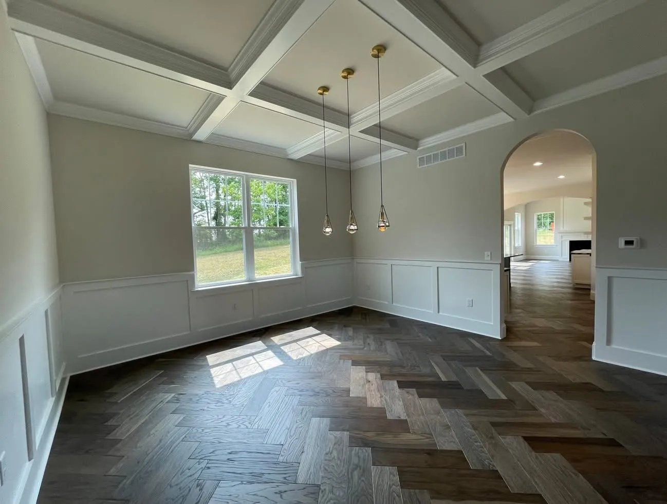 A dining room featuring a white coffered ceiling and white wainscoting with dark herringbone wood floors.