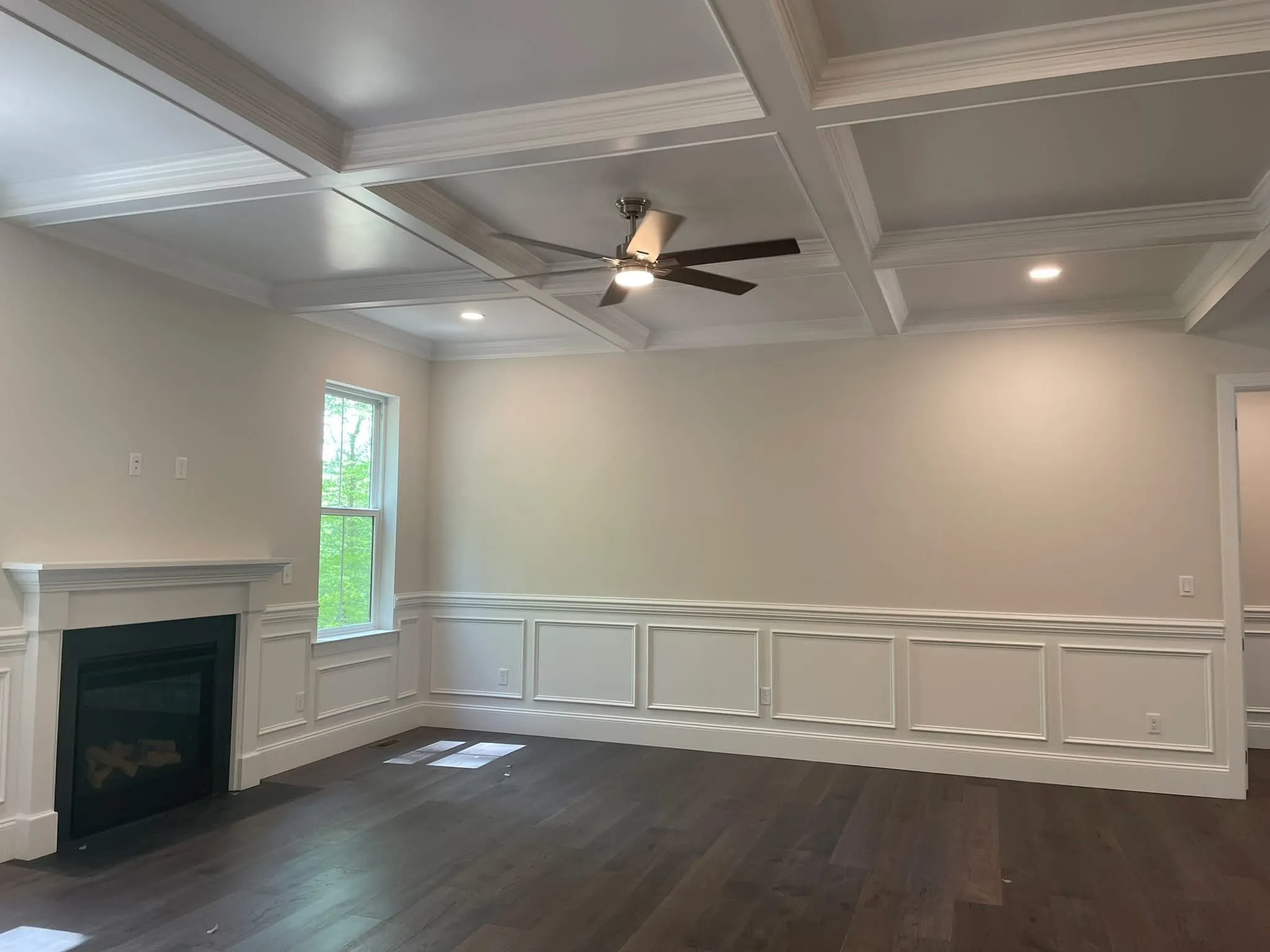 A living room featuring a white coffered ceiling and white wainscoting with a fireplace surround.