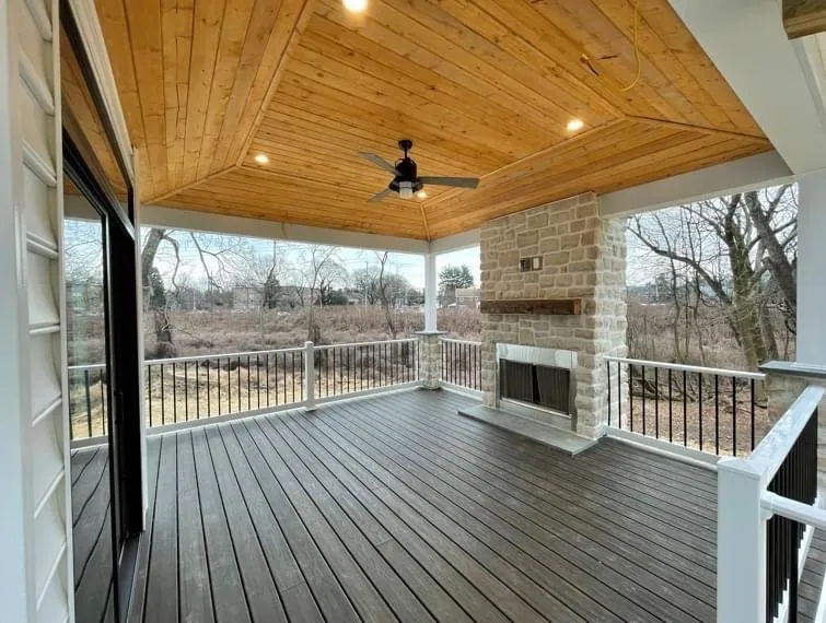 A covered deck featuring a natural wood tongue and groove ceiling and a stone fireplace.