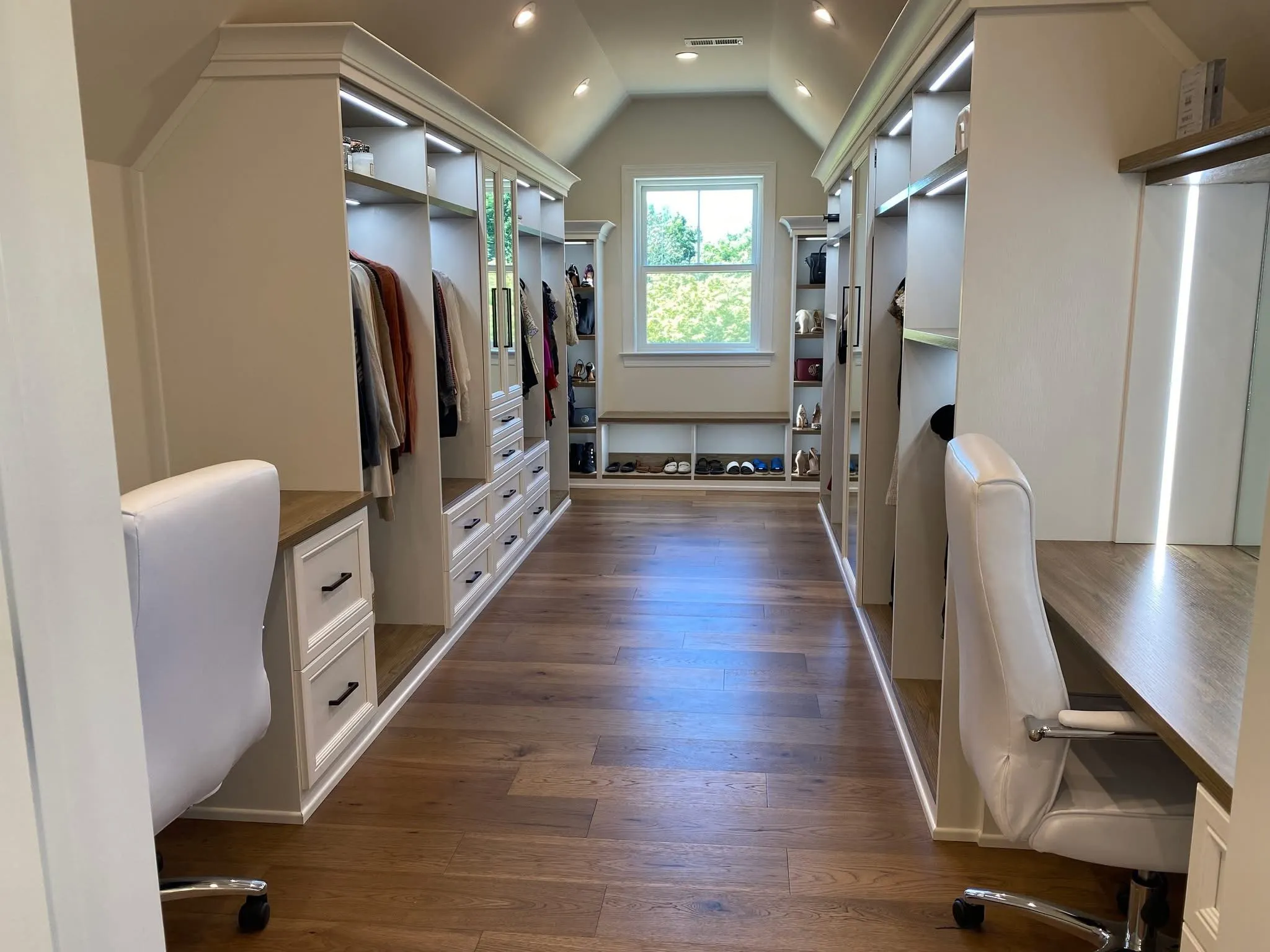 White walk-in closet cabinetry with integrated desks, shelving, and LED lighting in a vaulted room.
