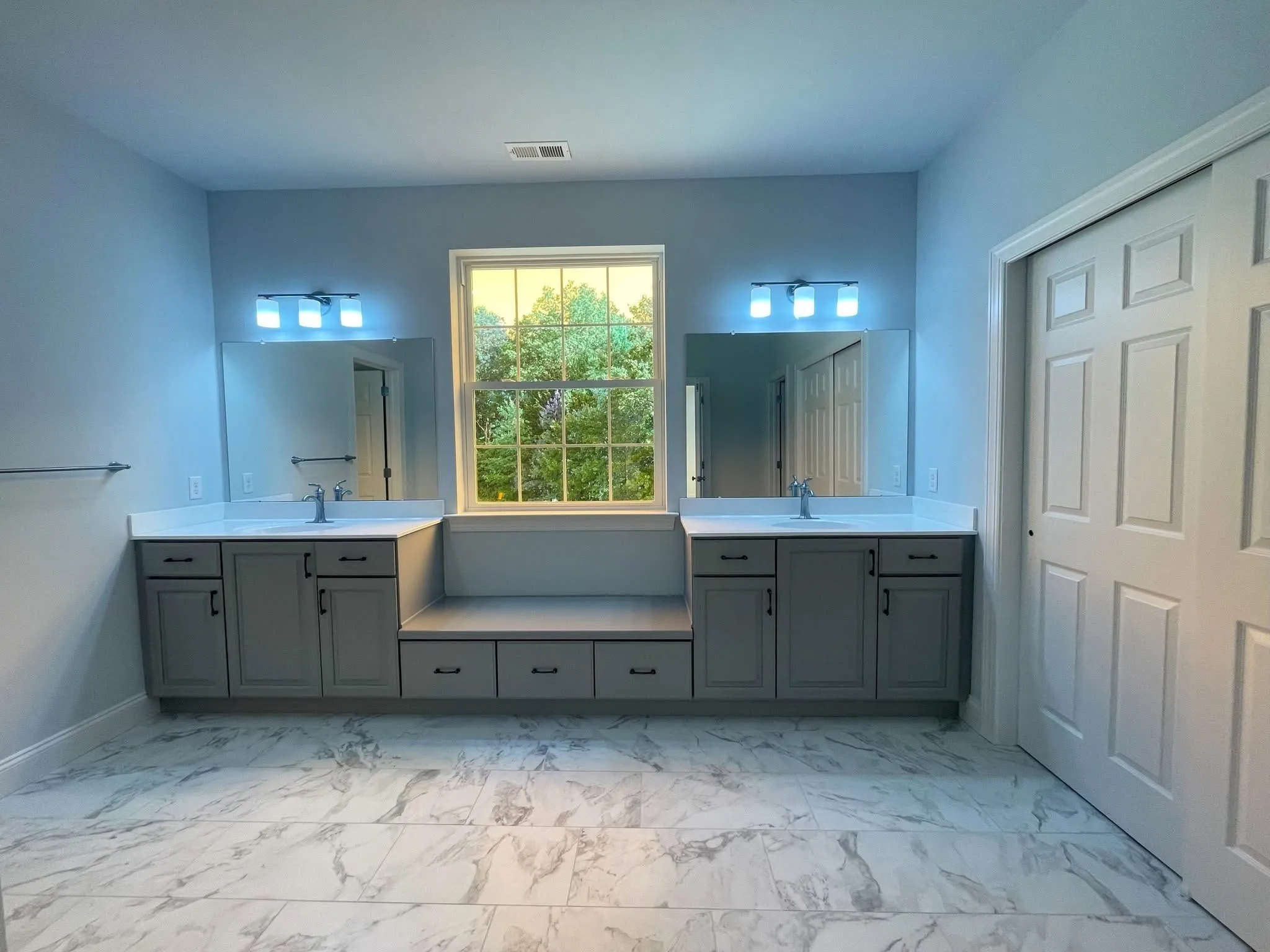 A double vanity bathroom cabinet set with a center bench and marble tile flooring.
