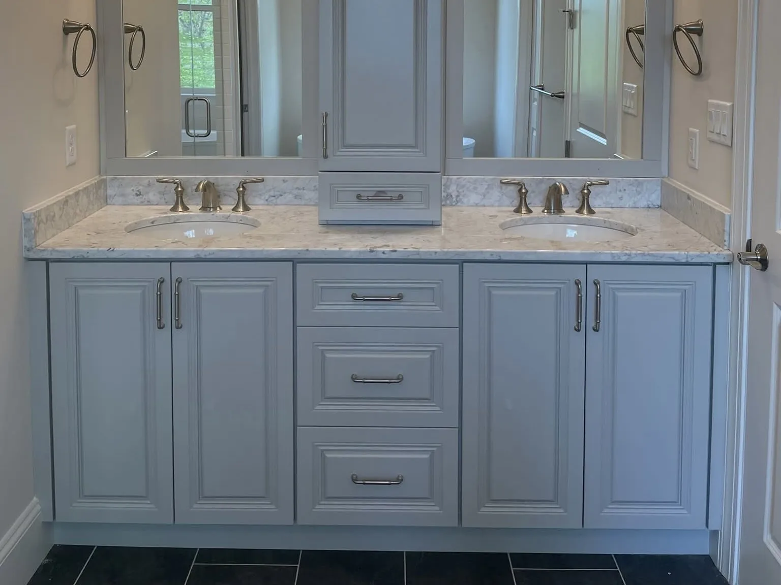 A gray double vanity with marble countertop and central tower cabinet in a bathroom.