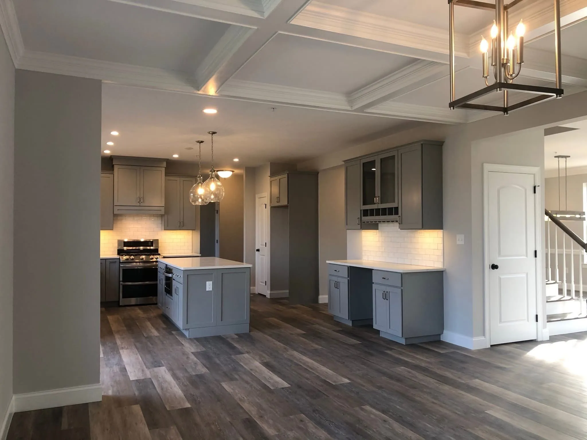 A modern kitchen features gray shaker cabinets, a central island, and a white coffered ceiling.