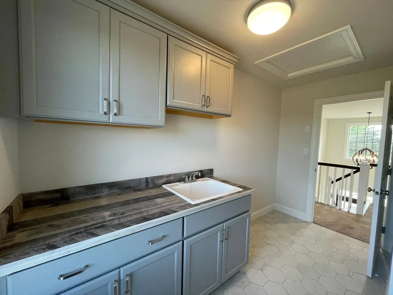 Gray shaker style cabinets with a rustic wood laminate countertop and integrated sink in a laundry room.
