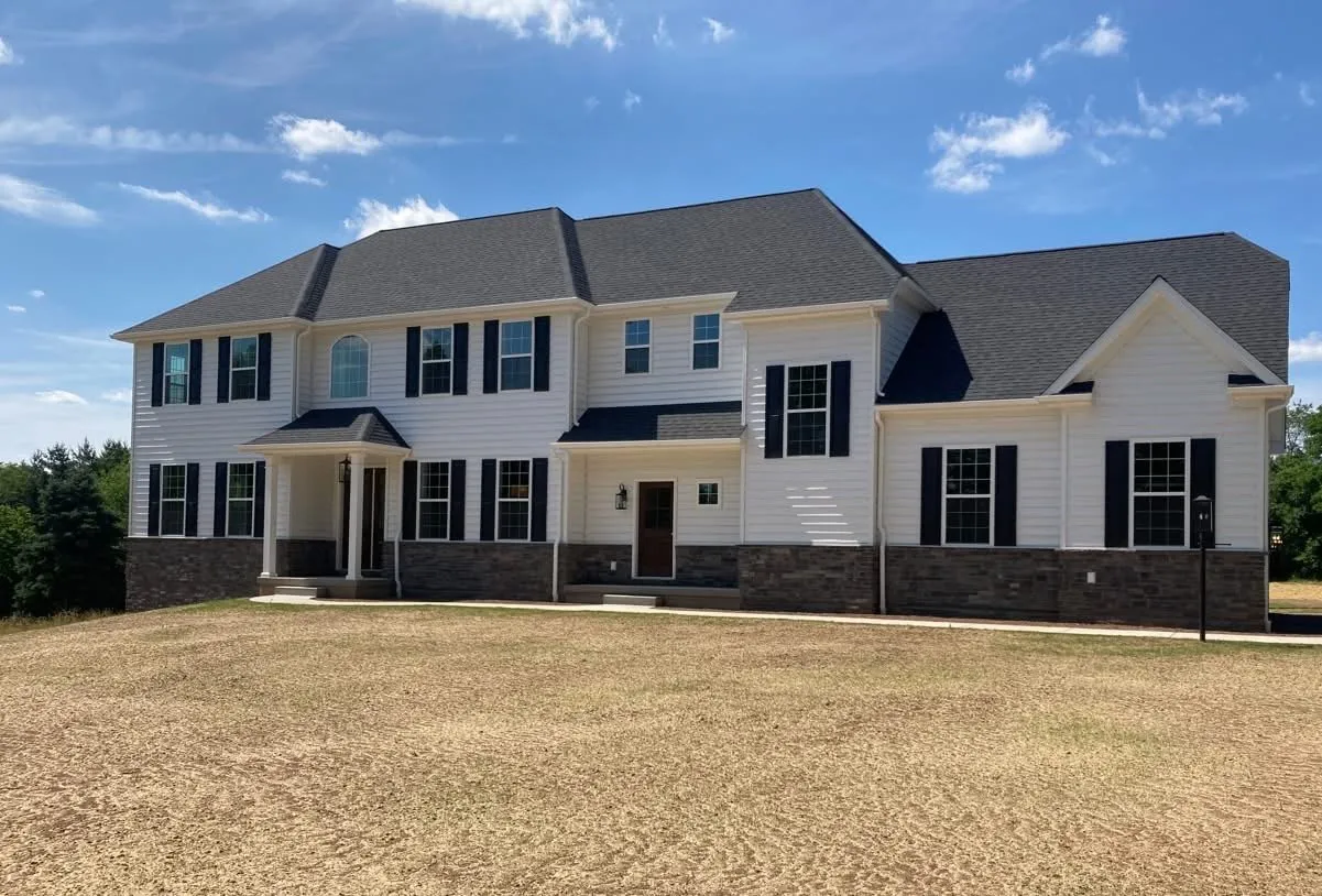 A large two-story colonial style home with white siding, stone veneer, and black shutters.