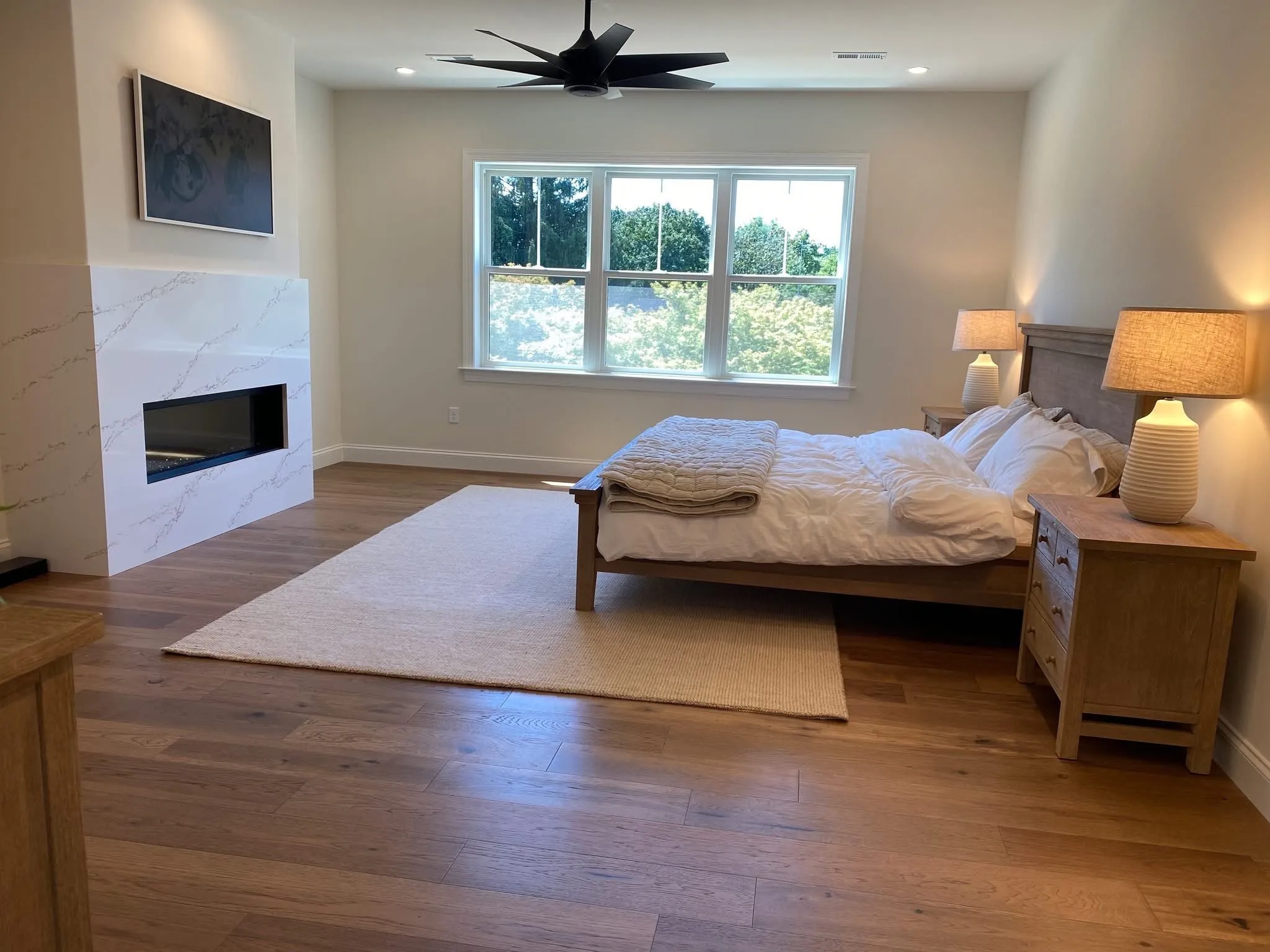 A modern bedroom features a sleek marble fireplace surround and hardwood floors in a new home.