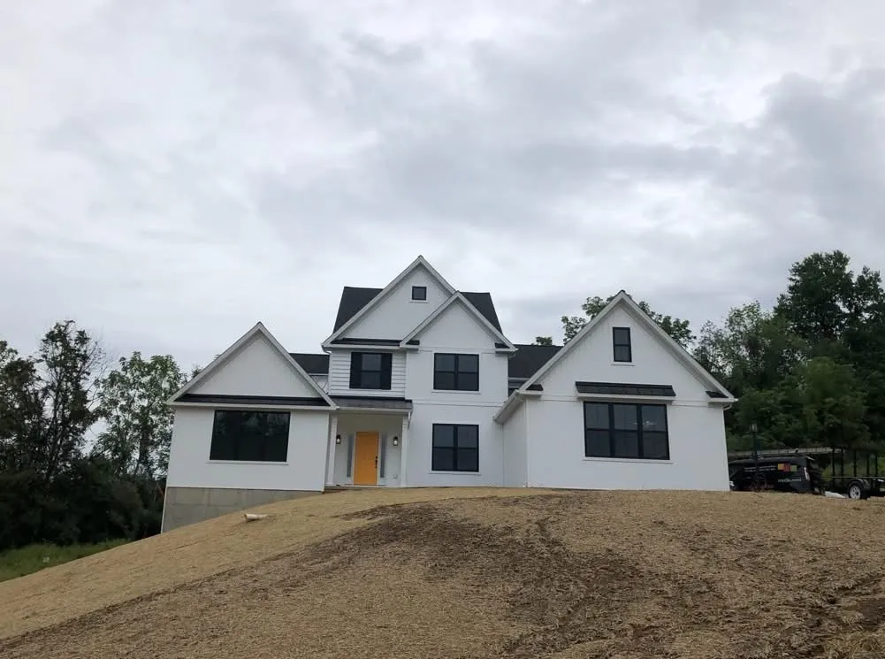 A modern farmhouse exterior features white siding, black window frames, and a bright yellow front door.