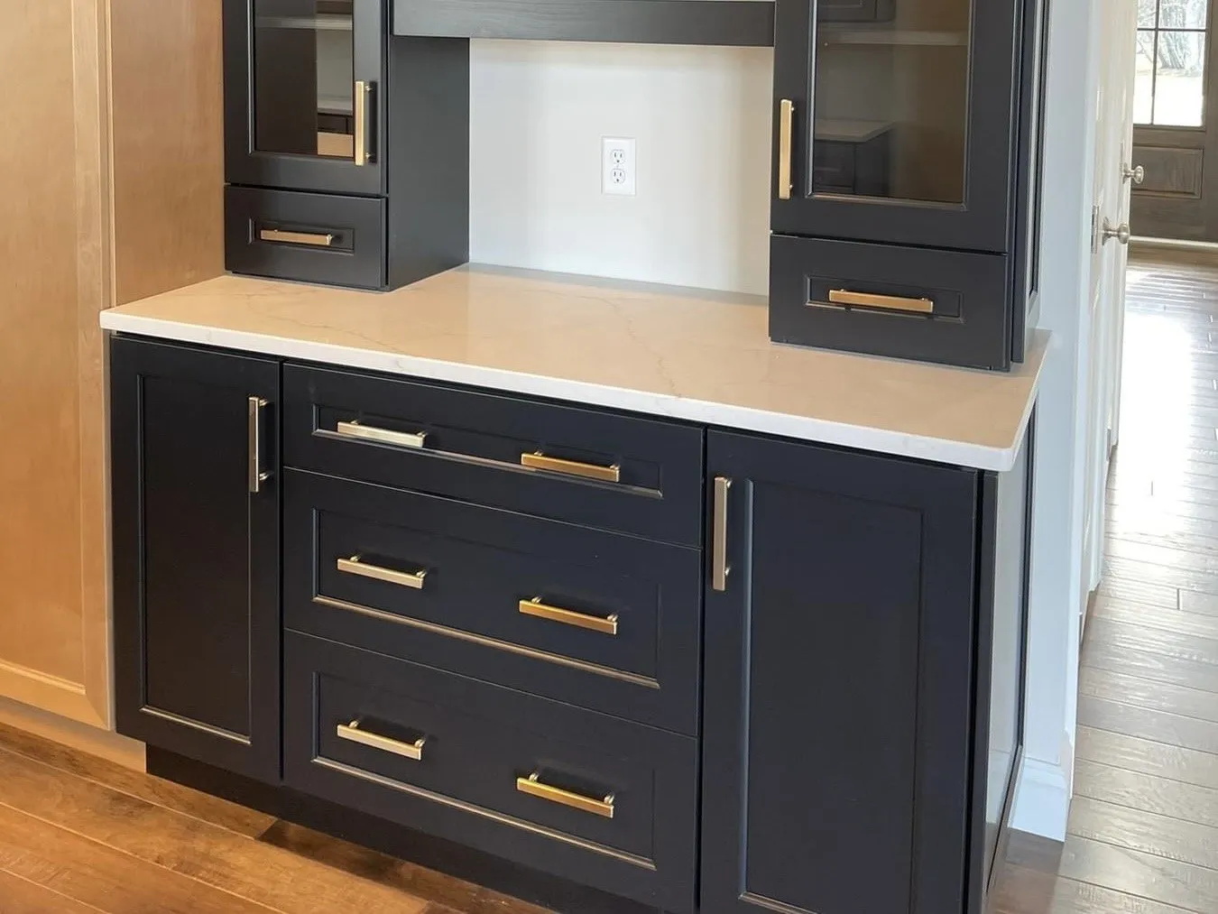 A navy blue kitchen coffee bar with quartz countertops and brass hardware in a home.