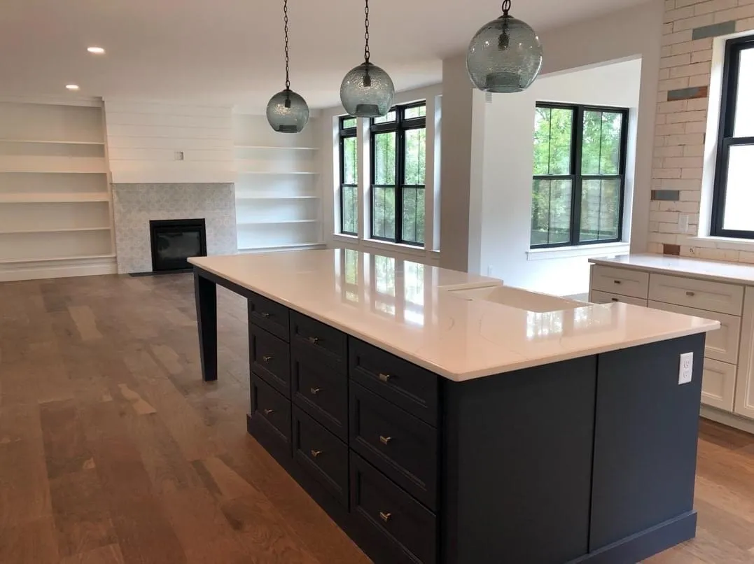 A navy blue kitchen island with quartz countertop sits before a white fireplace with built-in shelving.