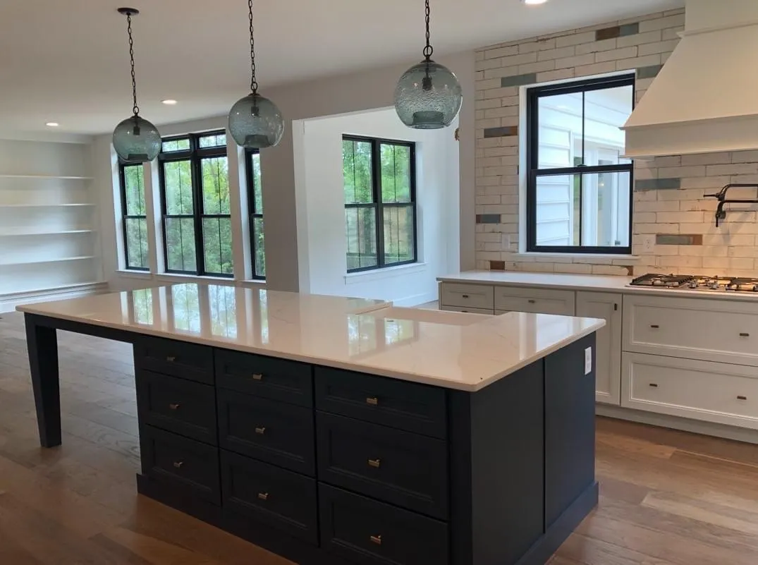 A kitchen featuring a large navy blue island with white perimeter cabinets and glass pendant lights.