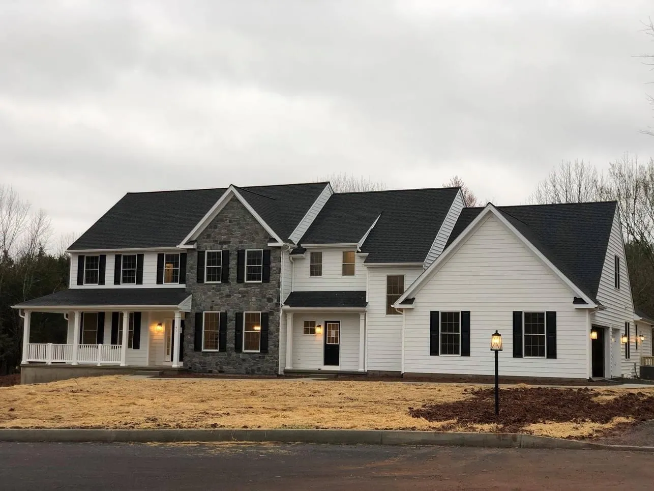 A newly constructed colonial style house with white siding, black shutters, and stone veneer accents.