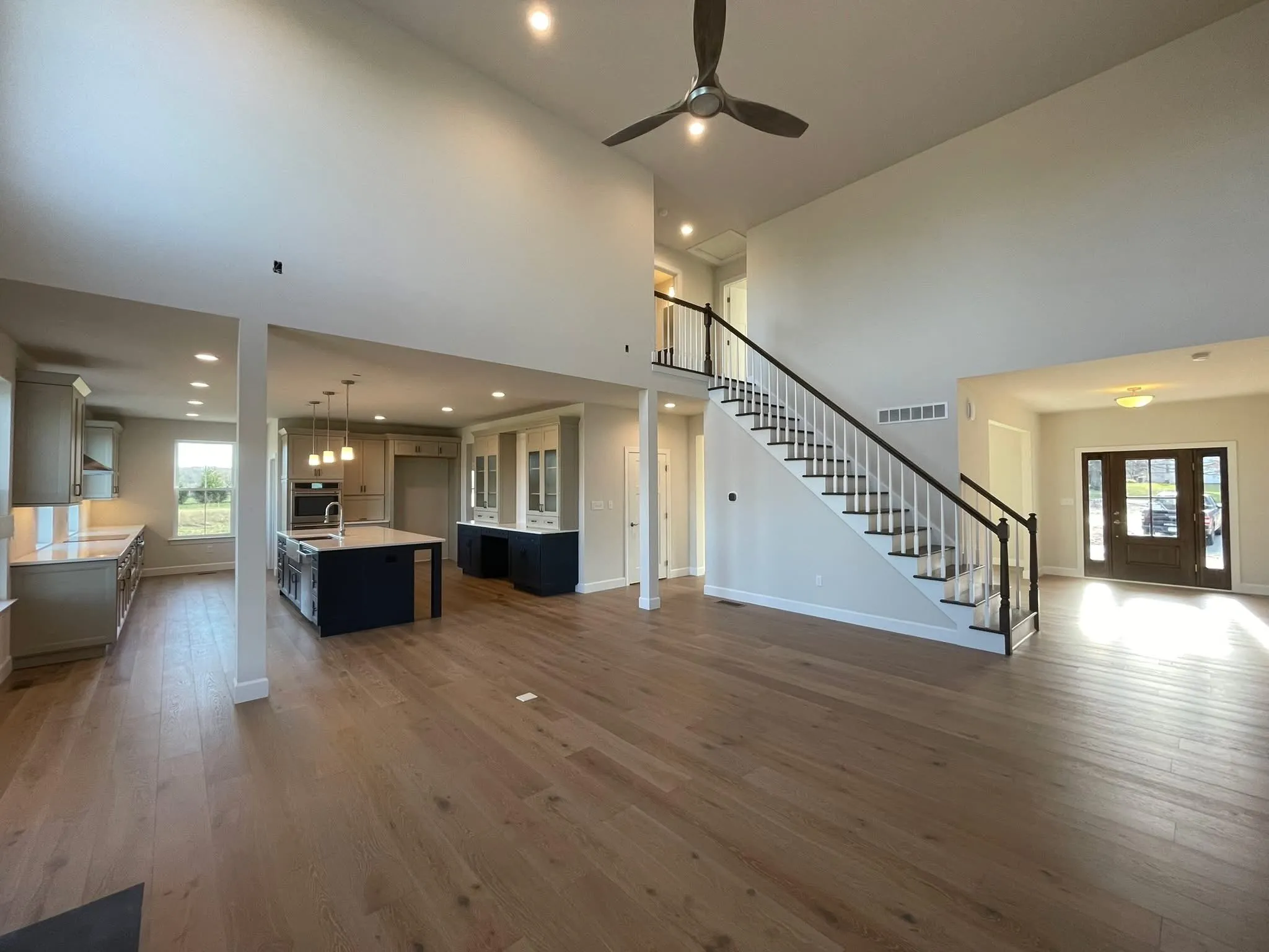 A two-story foyer and kitchen featuring a wooden staircase with white balusters and dark handrails.