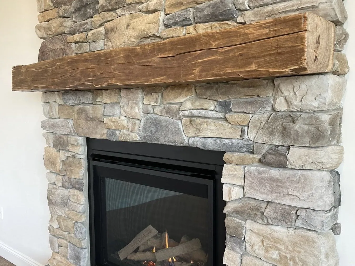 A rustic timber mantel is installed over a modern gas fireplace with stone veneer surround.