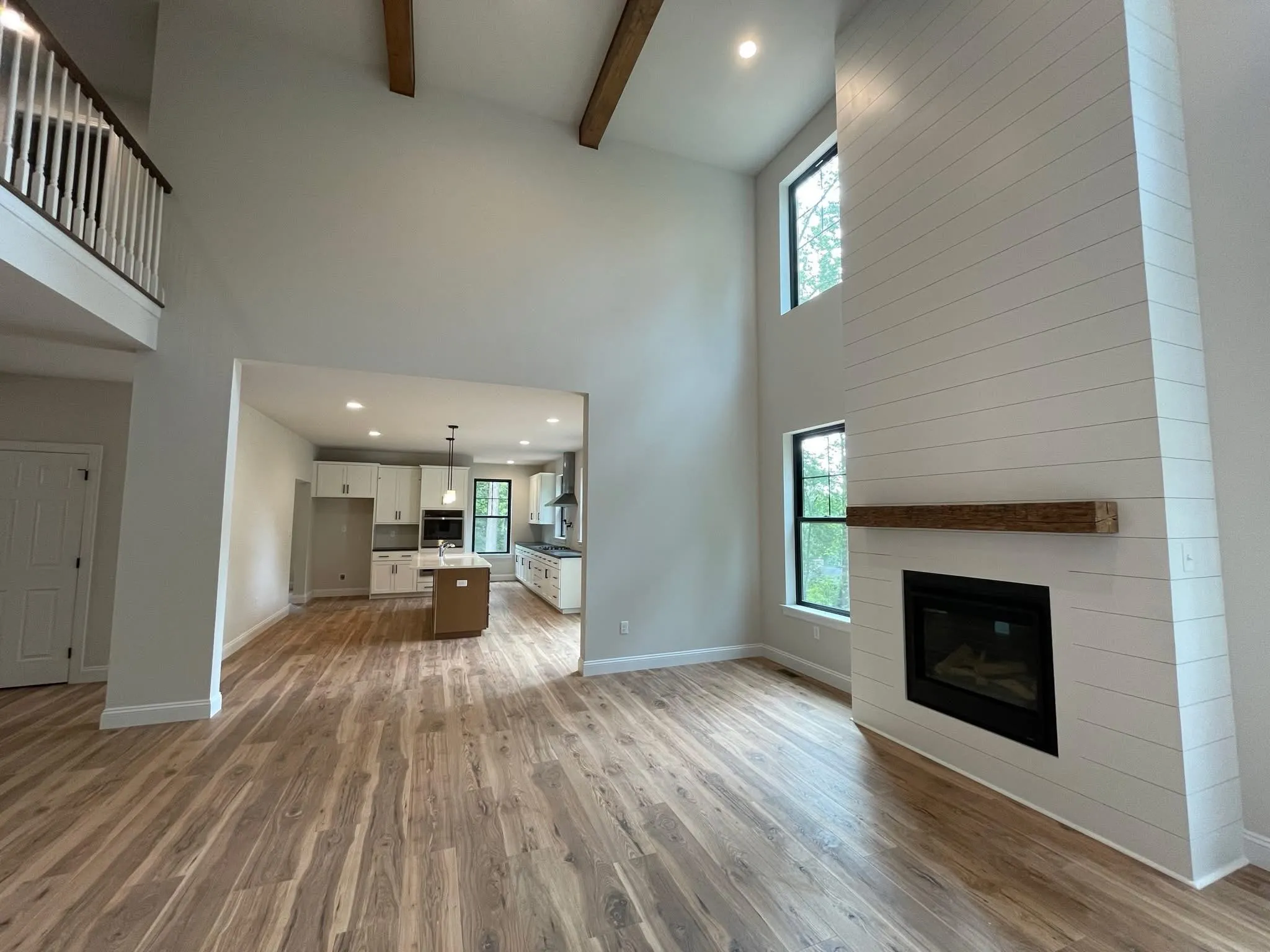 A two-story living room features a white shiplap fireplace surround with a rustic wood mantel.