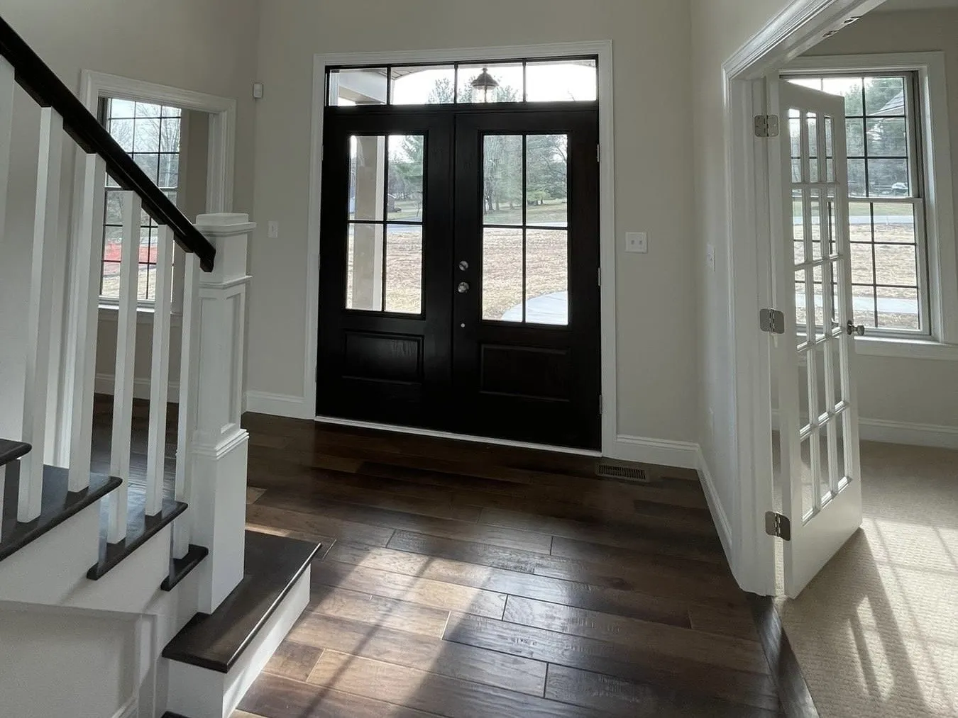 A white staircase with dark treads and a black double front door in a foyer.