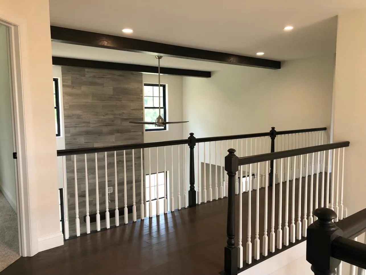 A wooden staircase railing with white balusters overlooks a two-story room with dark ceiling beams.