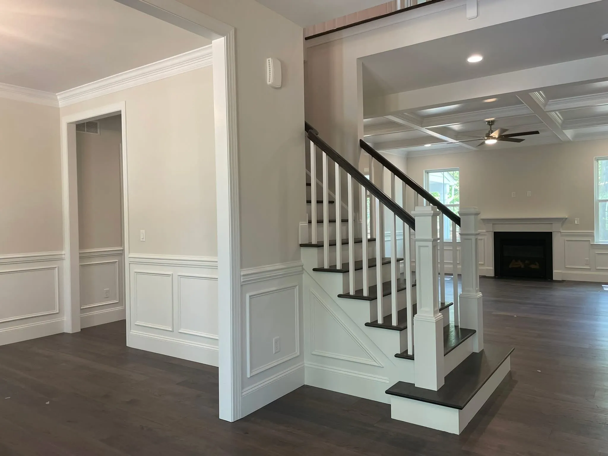A staircase with dark wood treads and white balusters sits beside walls with recessed wainscoting.