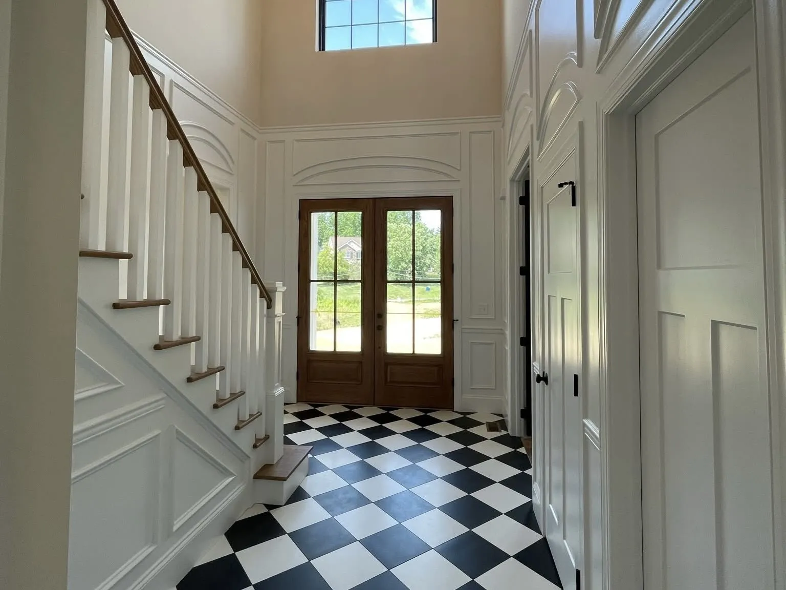 A two-story foyer featuring white wainscoting, a wooden staircase, and black and white checkered flooring.
