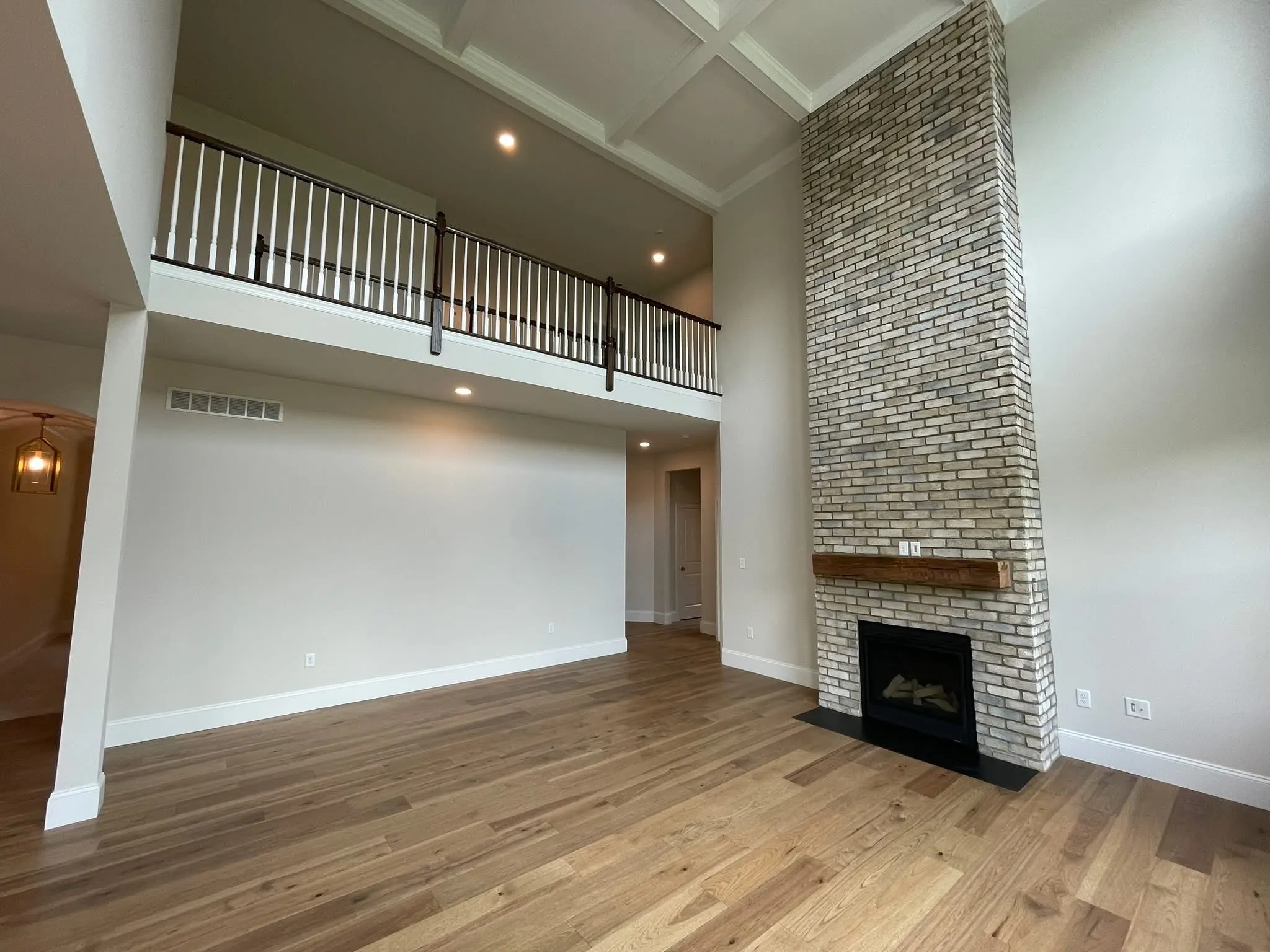 A two-story living room featuring a floor-to-ceiling brick fireplace and a white coffered ceiling.