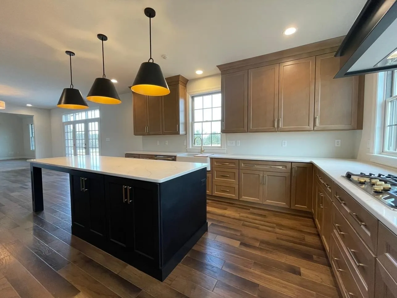 A modern kitchen featuring light wood cabinets, a black kitchen island, and white quartz countertops.