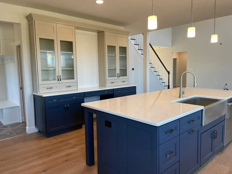 A kitchen featuring a navy blue island with a farmhouse sink and a two-tone hutch cabinet.