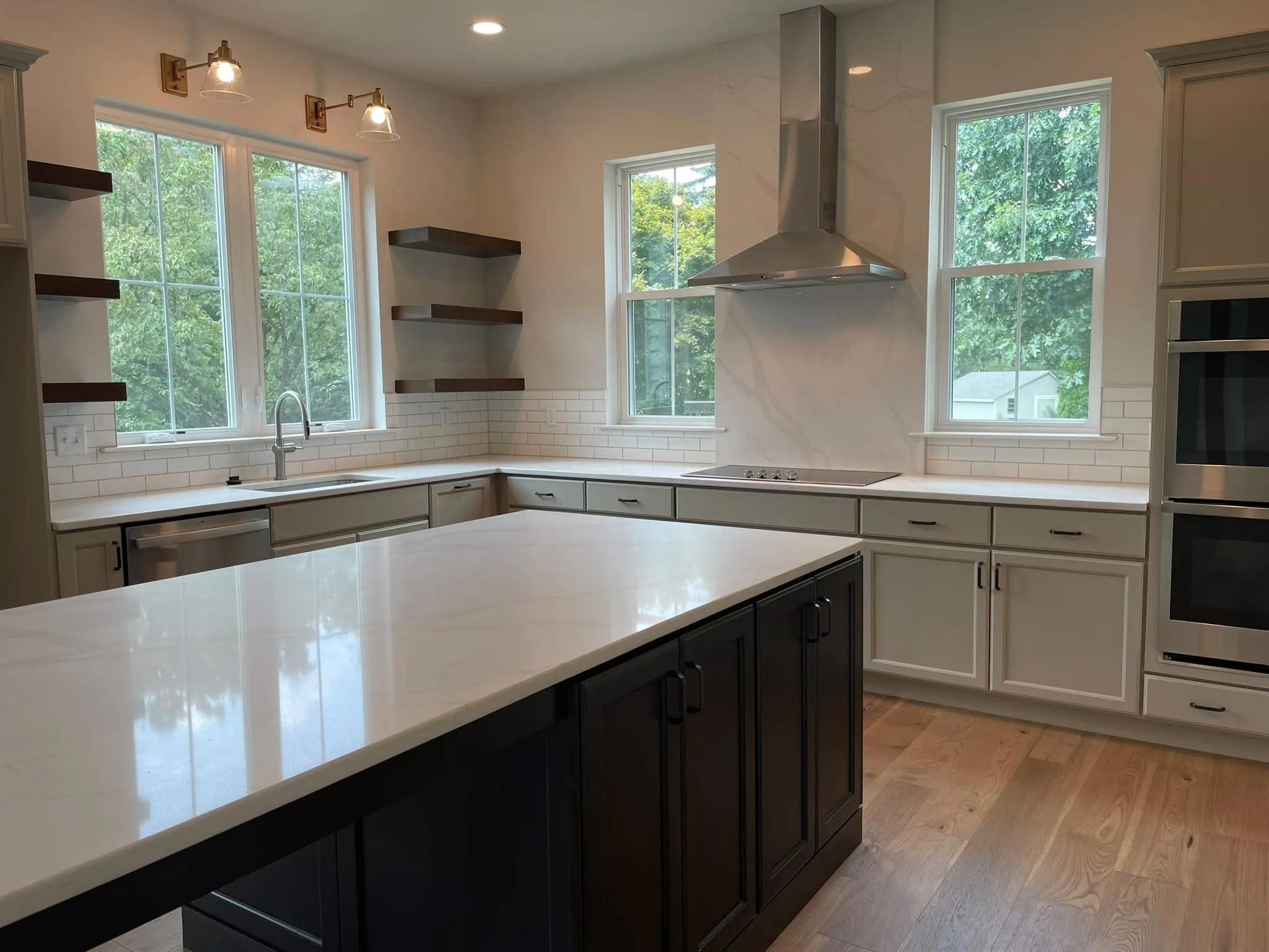 A modern kitchen featuring light gray perimeter cabinets, a dark island, and floating wood shelves.