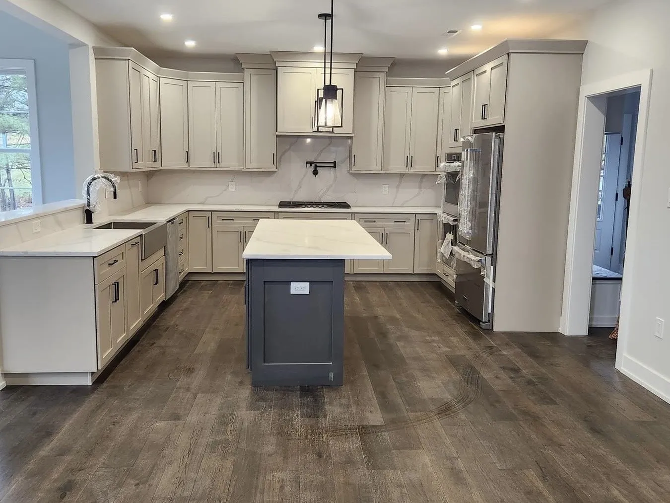 A kitchen featuring light beige perimeter cabinets and a dark gray center island with white countertops.