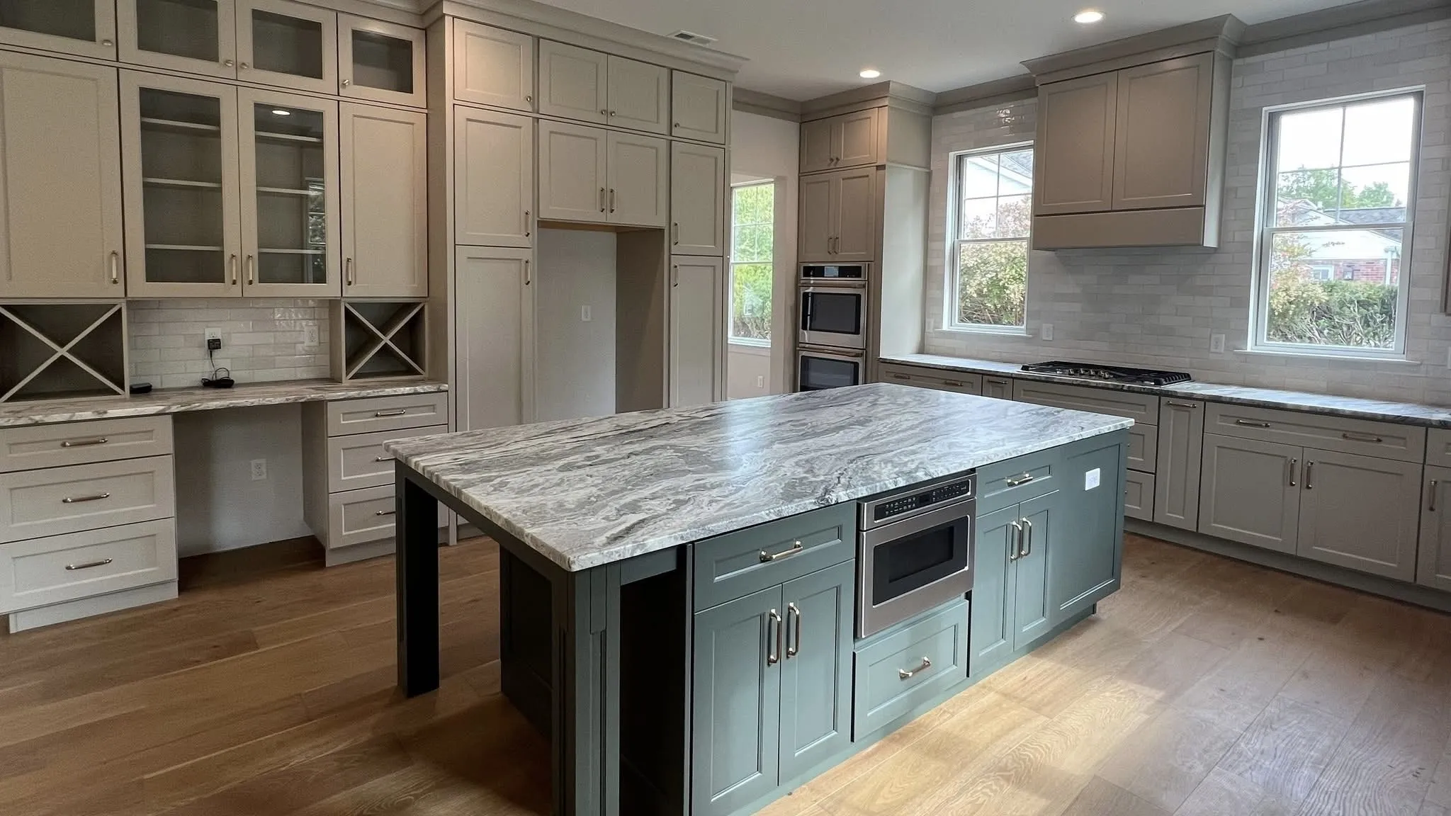 A kitchen featuring light grey perimeter cabinets, a dark green island, and marble countertops.