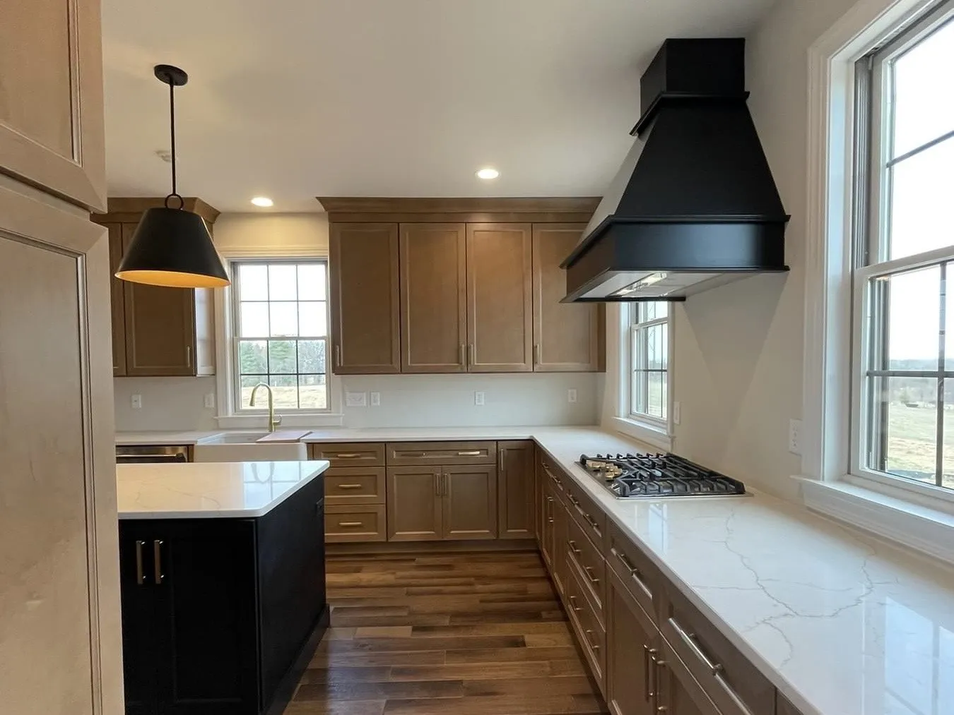 A modern kitchen features wood cabinets, a black island, white countertops, and a black range hood.