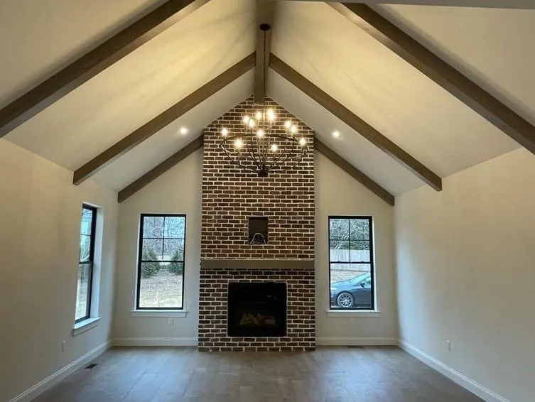 A vaulted ceiling with exposed wooden beams above a floor-to-ceiling brick fireplace in a living room.