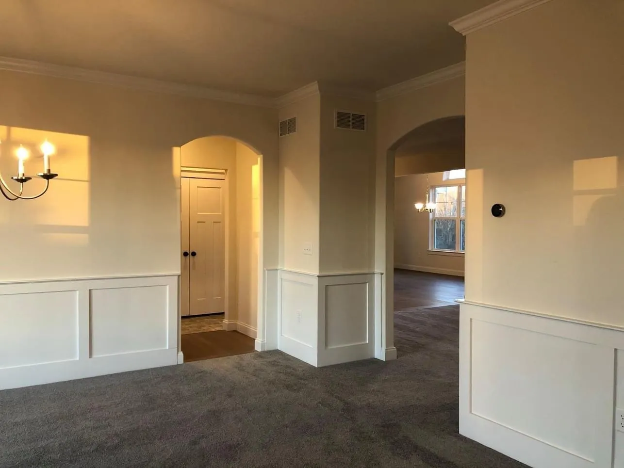 White wainscoting panels line the walls of a room featuring arched doorways and crown molding.