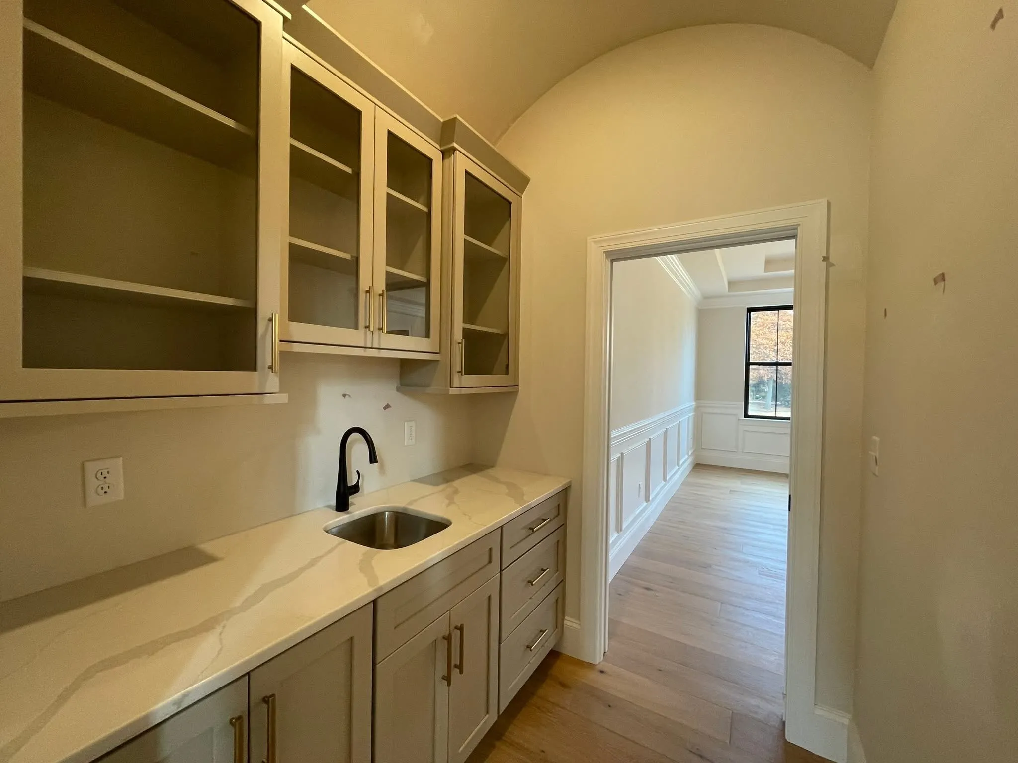 A wet bar with light gray cabinets, glass upper doors, and a white quartz countertop.