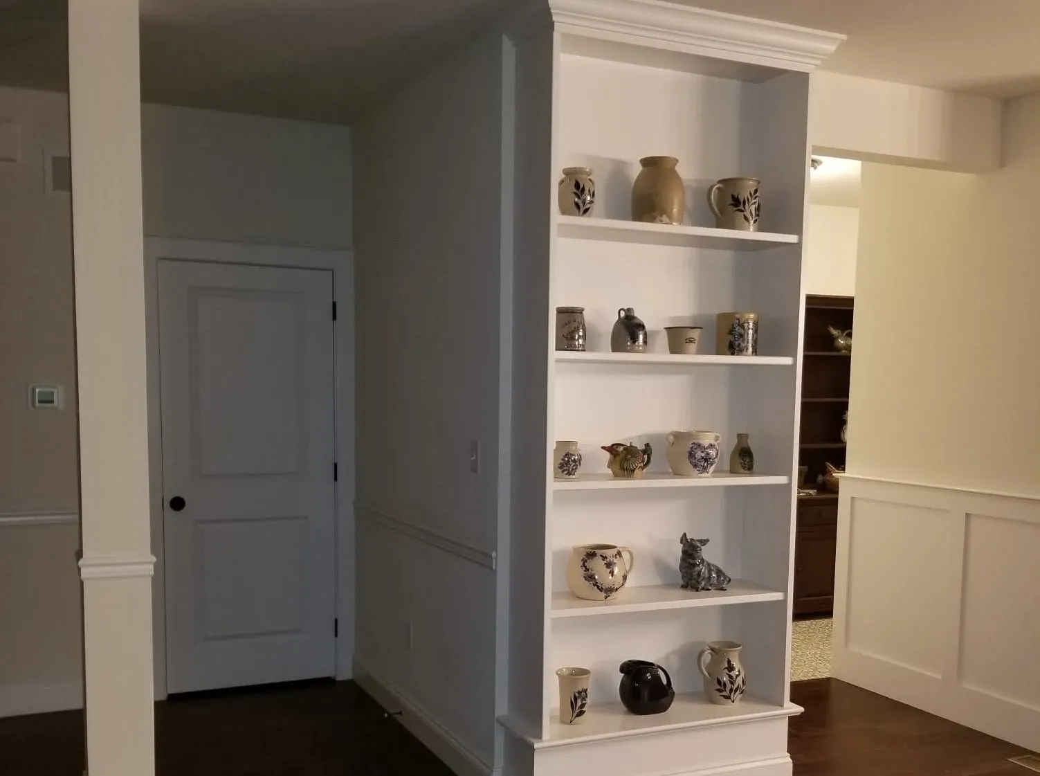 A white built-in bookcase stands next to a doorway with wainscoting on the wall.