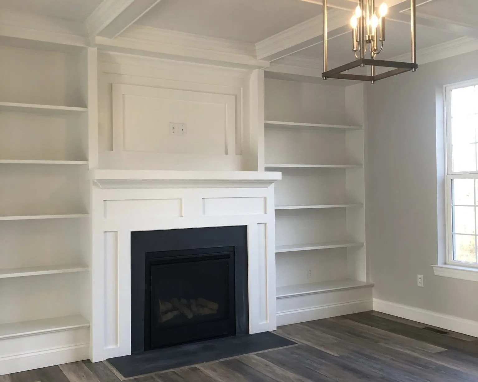 A white fireplace mantel flanked by built-in shelving units in a modern living room.