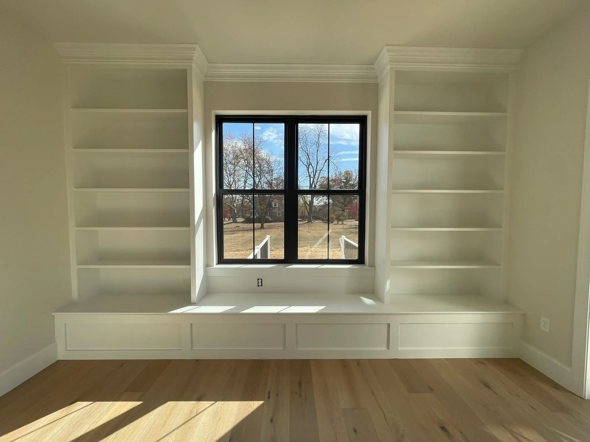 White built-in bookcases flank a central window with a matching bench seat and crown molding.