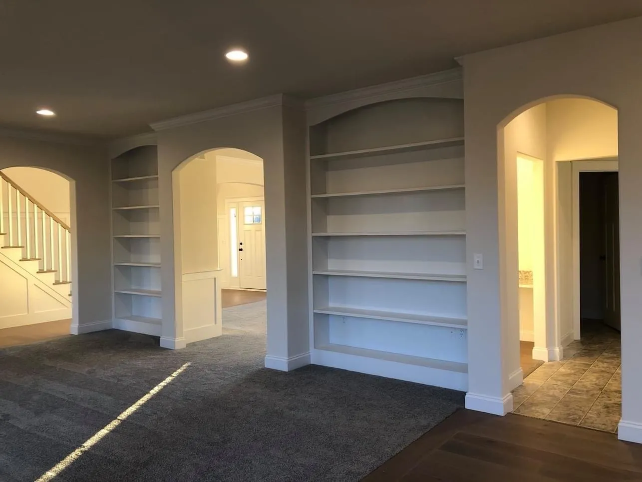 White built-in shelving units installed within arched wall openings in a residential living space.