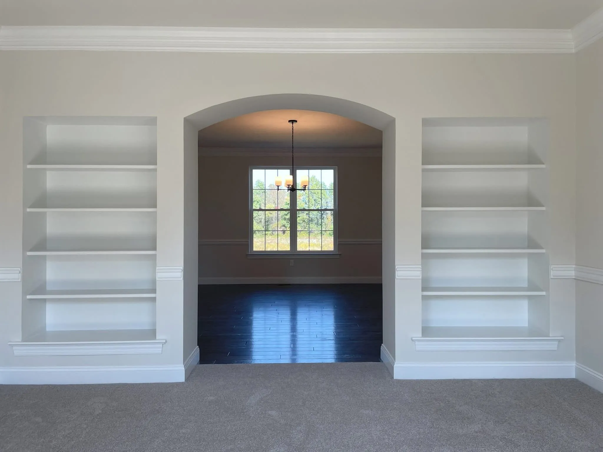 Symmetrical white built-in bookshelves flank an arched passageway leading into a dining room with hardwood floors.