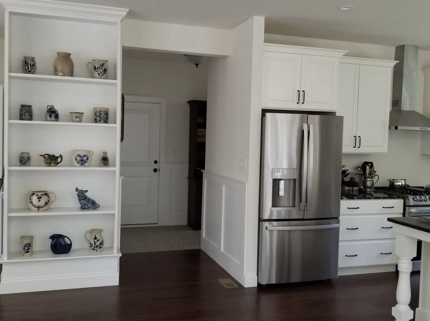 White built-in shelving unit next to a kitchen refrigerator with white wainscoting on the wall.