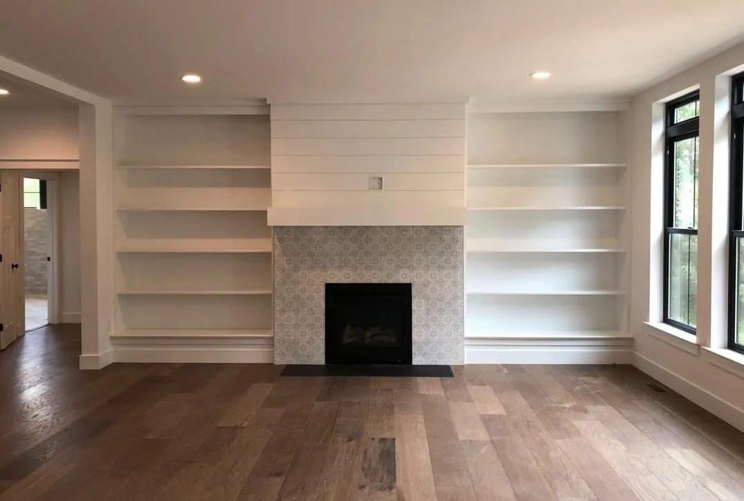 White built-in bookshelves flank a fireplace with a patterned tile surround and shiplap detail.
