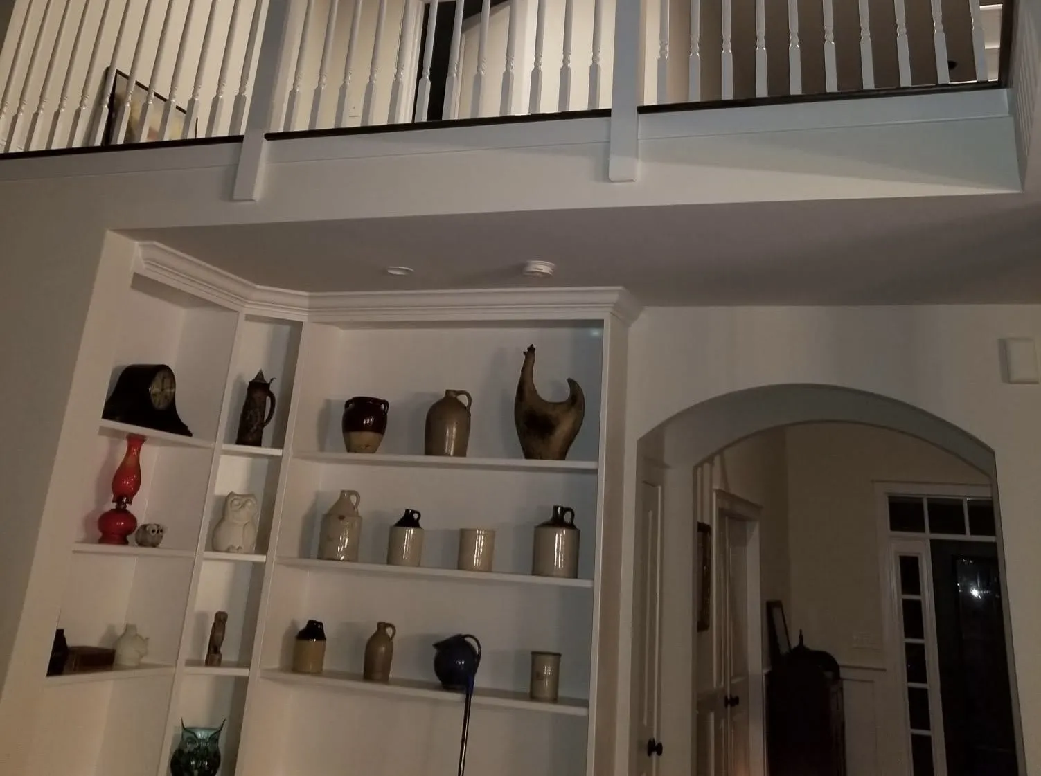 White built-in shelving units installed beneath a white wooden staircase railing in a residential home.