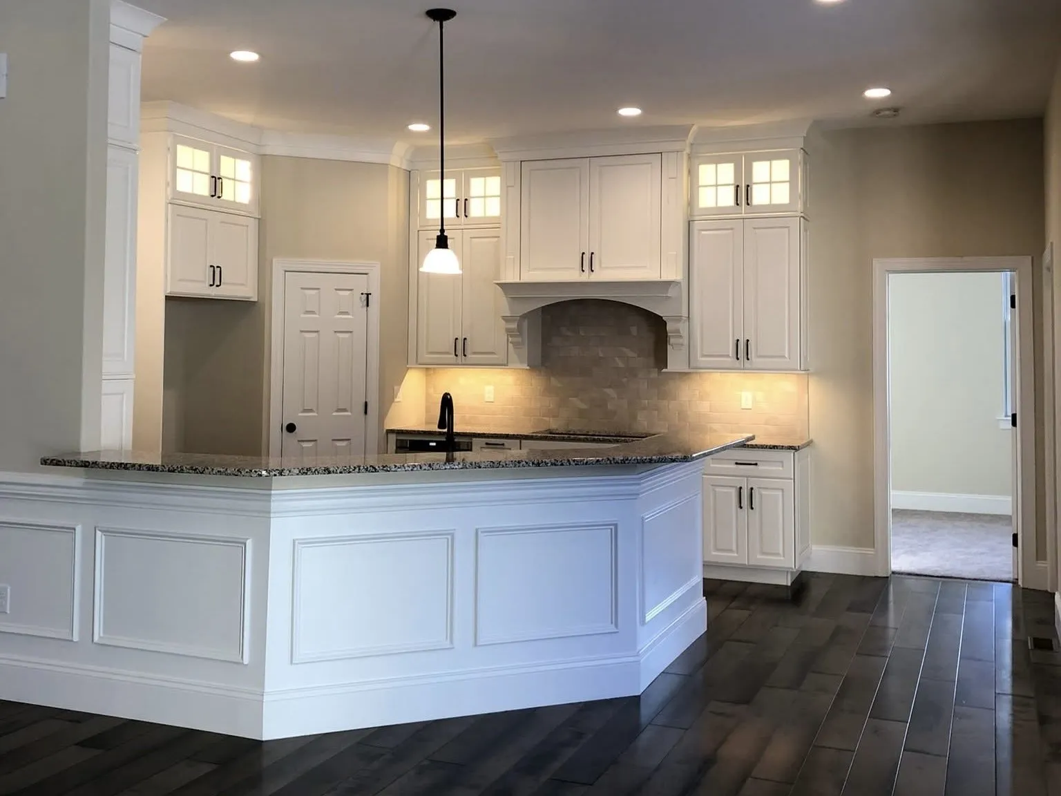 White kitchen cabinets with glass upper doors and a wainscoted peninsula island in a home.
